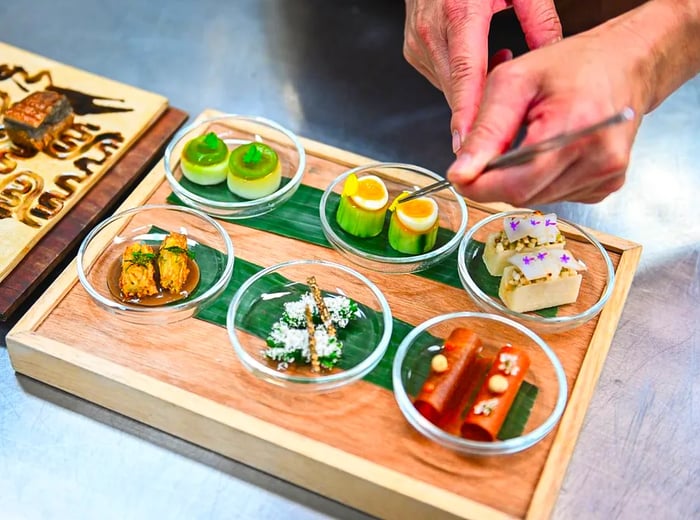 A chef meticulously arranges vibrant dishes on a platter using tweezers.