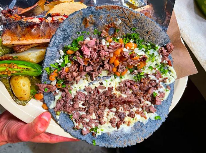 An aerial view of a taco overflowing with meat, melted cheese, beans, and cabbage, displayed alongside other delicious items.