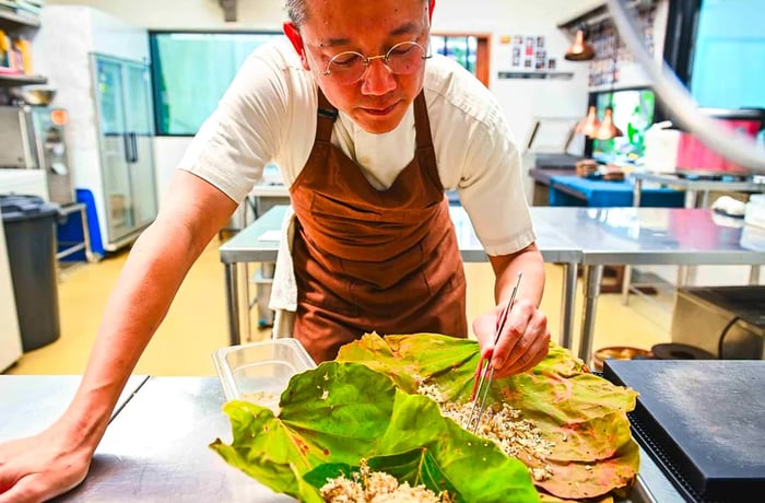 A chef bends down, carefully using tweezers to handle large leaves teeming with eggs.