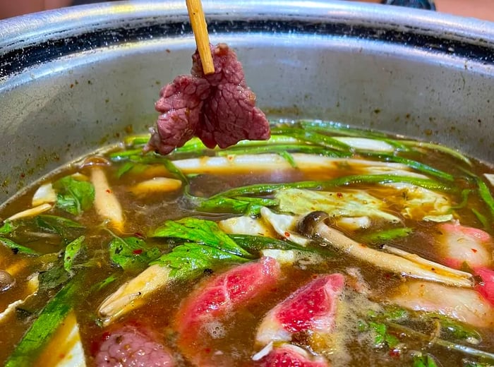 A pair of chopsticks holds a small piece of meat over a pot of simmering jaew hon.