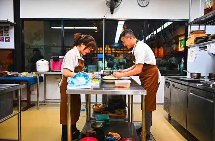 Two chefs collaborate at a prep table, each focused on their tasks.