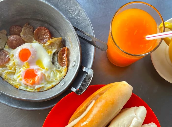 A skillet of fried eggs served with bread rolls and juice.