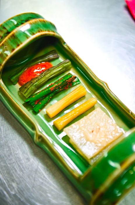 A green tray designed to mimic a stalk of bamboo showcases a variety of vegetable dishes.