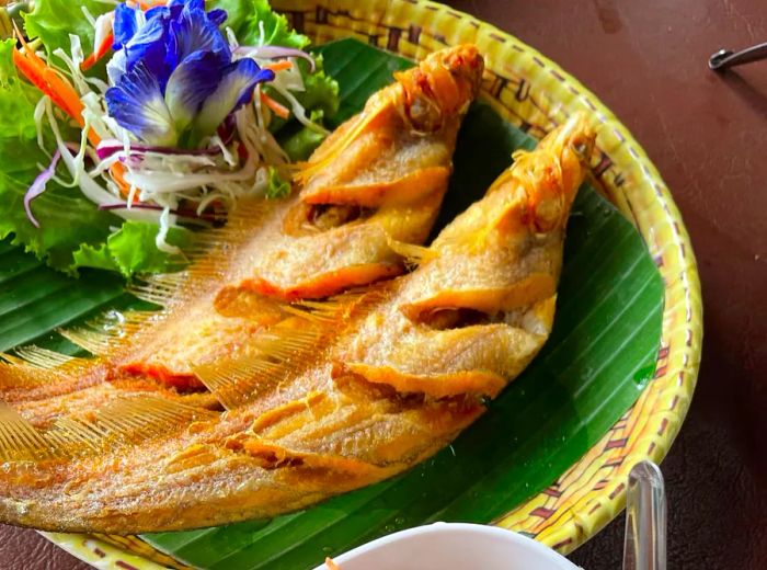 A basket holding two whole fried fish accompanied by two salads.