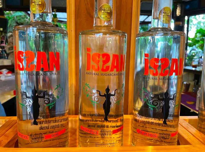 Three clear rum bottles labeled Issan featuring a silhouetted figure.