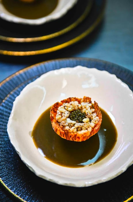 An artistic presentation of ant eggs and caviar elegantly arranged in a small pastry shell, surrounded by sauce.