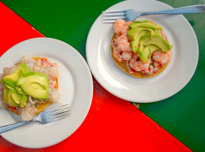 Plates of shrimp tostadas adorned with toppings and avocado slices.