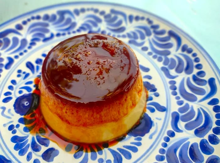 A beautifully presented slice of flan drizzled with sauce on a decorative plate.