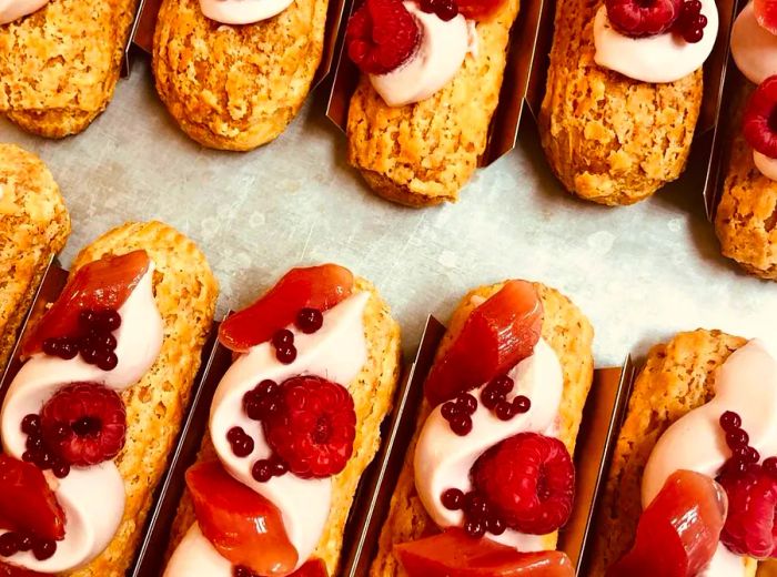 Aerial view of elegantly decorated eclairs topped with rhubarb slices and raspberries.