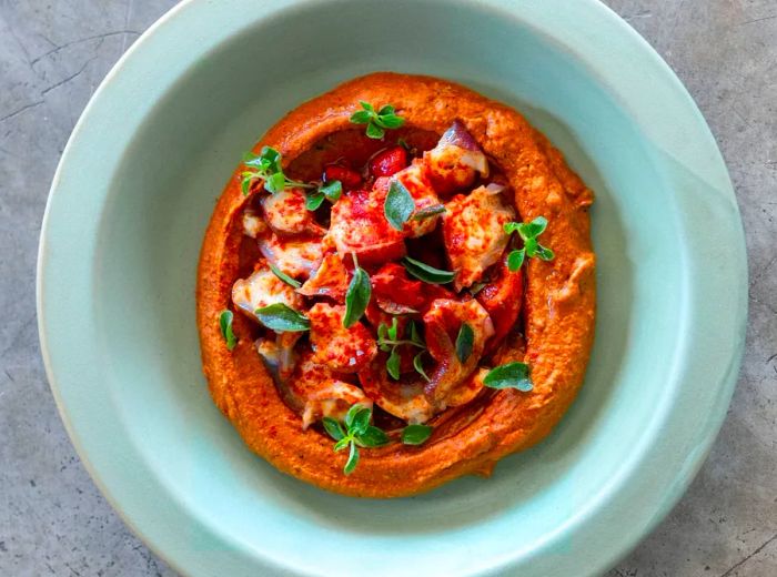 An aerial view of a bowl of muhammara garnished with pieces of octopus.