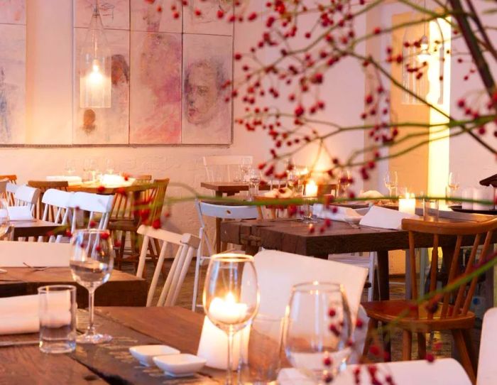 The restaurant's interior is awash in pink, featuring a striking floral arrangement, wall illustrations of people, and dinner tables adorned with candles.