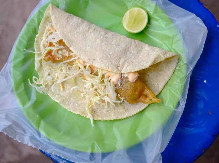 A crispy fish taco served on a plastic-lined plate with a wedge of lime.