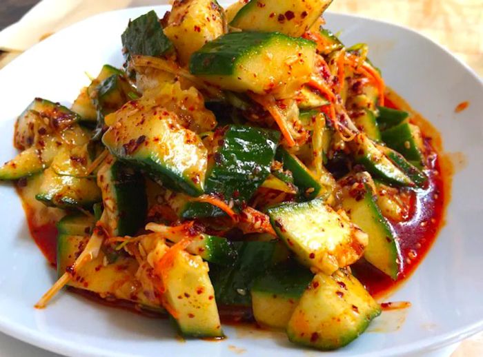 A plate generously filled with sliced cucumbers drizzled in red sauce.