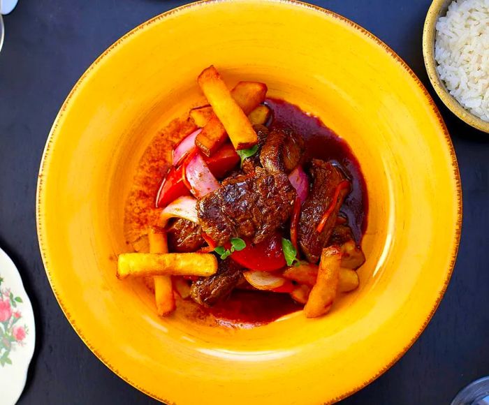 From above, a vibrant yellow bowl brimming with steak, french fries, onions, and sauce.