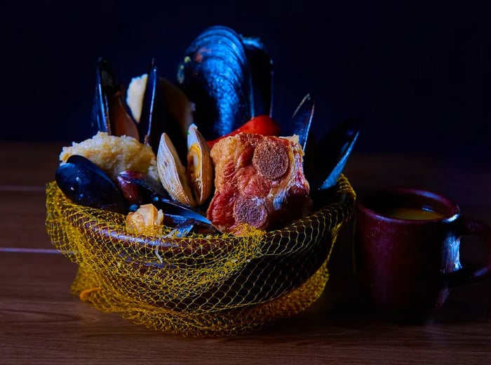 A bowl brimming with shellfish and pork ribs, elegantly presented and wrapped in a decorative net.