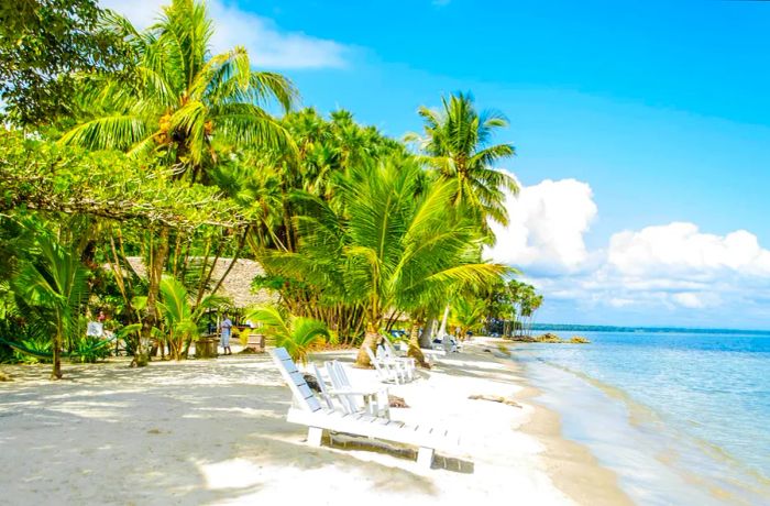 White lounge chairs and palm trees dotting the shore at Playa Blanca, Guatemala