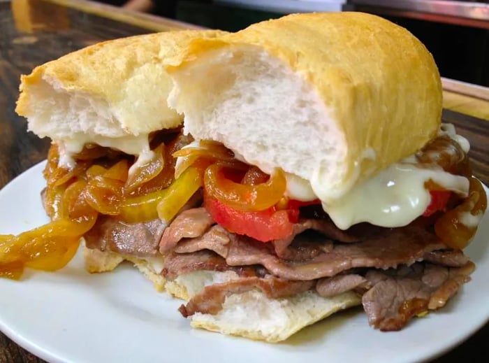 A hearty sandwich filled with sliced beef, sautéed onions, tomatoes, and sauce, all served on thick bread.