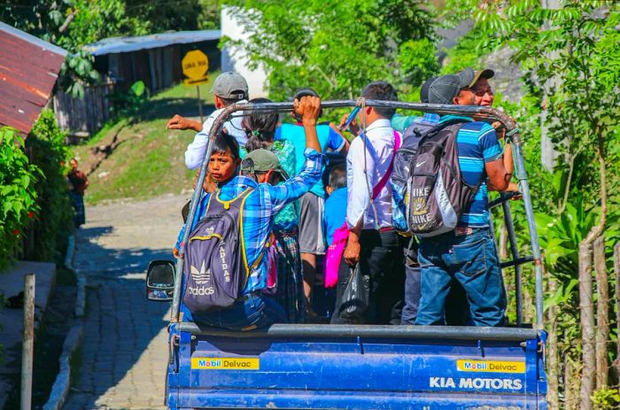 A group of individuals standing in the flatbed of a pickup truck on a road in Guatemala.