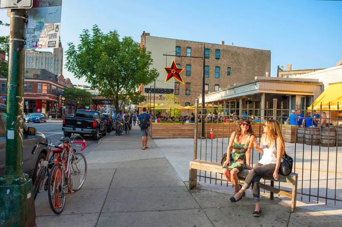 Two young women relax on a bench at the entrance of Big Star restaurant in Chicago on a sunny evening.