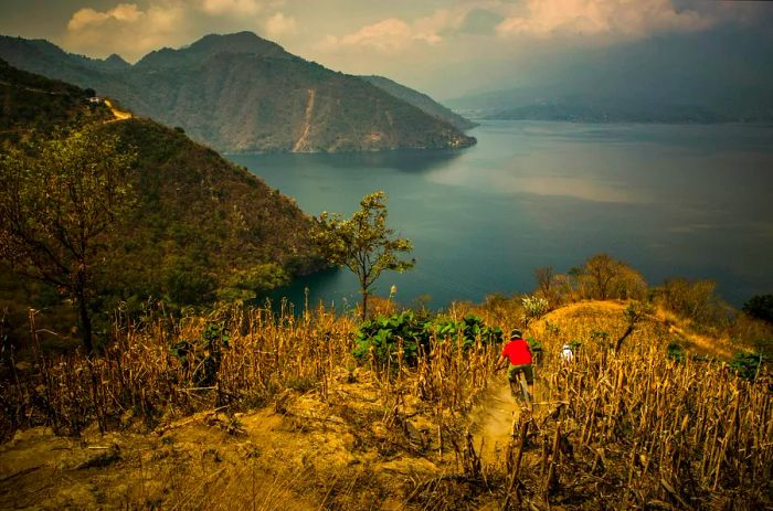 Two mountain bikers navigating a steep single track that leads down toward a lake in Guatemala.