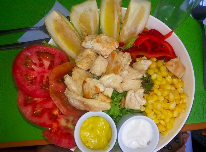 Aerial view of a plate featuring chicken slices surrounded by tomato, corn, peppers, lemon, and various sauces.