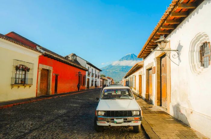 The front of a white pickup truck parked on a cobbled street in Antigua, with a mist-covered volcano in the background.