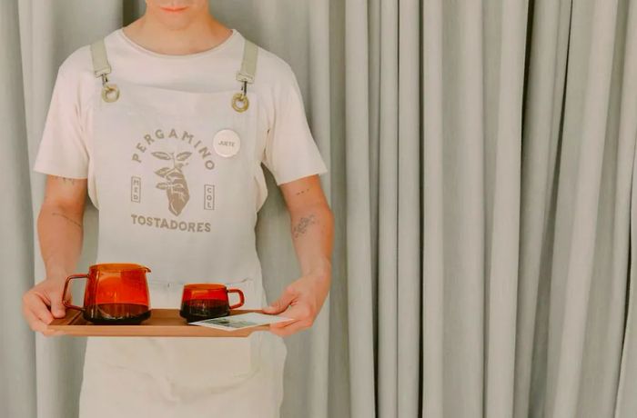 A server balances a tray featuring a semi-transparent pot and cup of coffee.