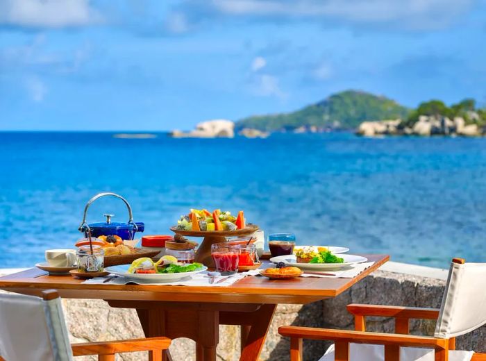 A beautifully arranged table featuring a selection of breakfast dishes on a deck that overlooks the ocean and surrounding islands.