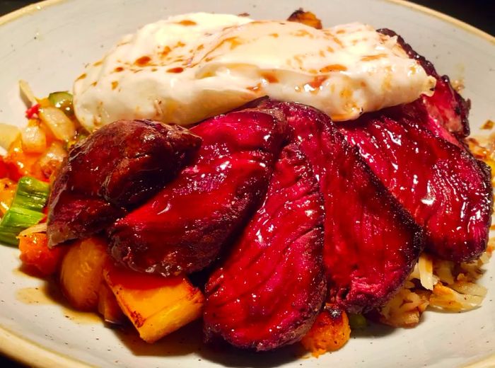 Rich red slices of filet served atop a medley of squash, asparagus, bell peppers, and onions, crowned with a fried egg.