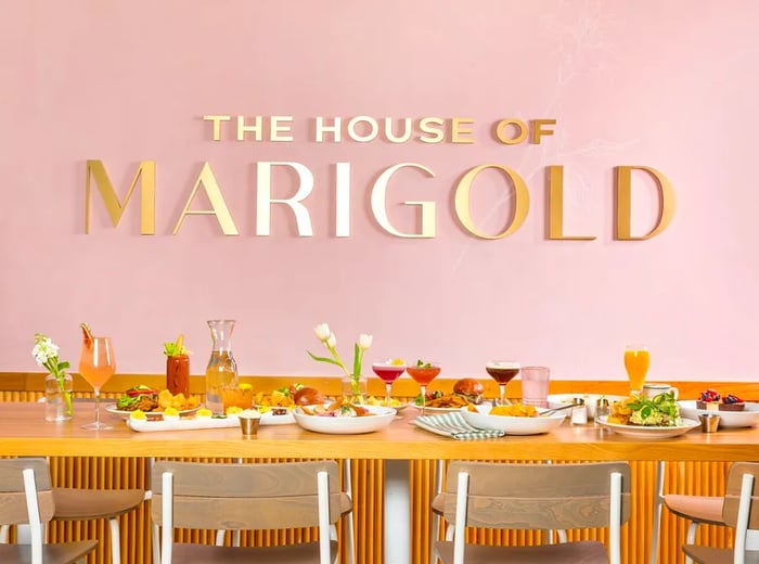 A beautifully arranged table showcasing a variety of dishes and beverages, set against a backdrop featuring a sign that reads “The House Of Marigold.”