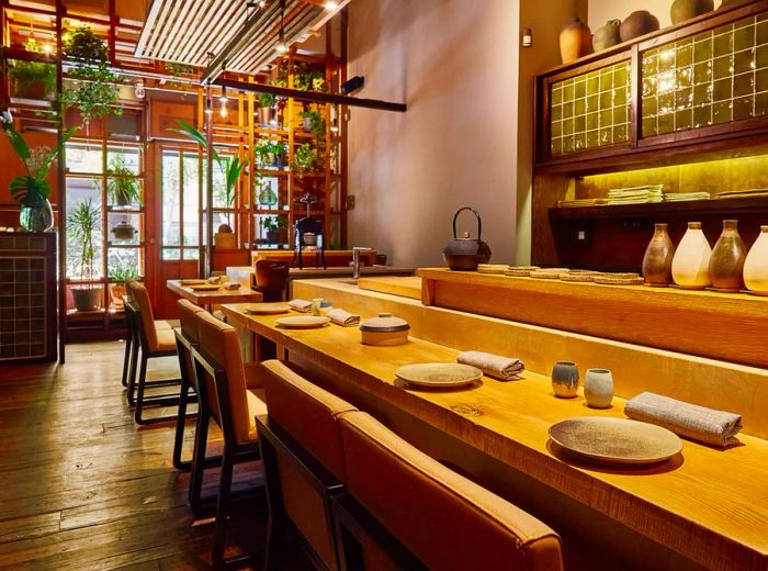 The interior of the restaurant features a sushi counter with place settings, and a bright entrance adorned with potted plants on shelves.