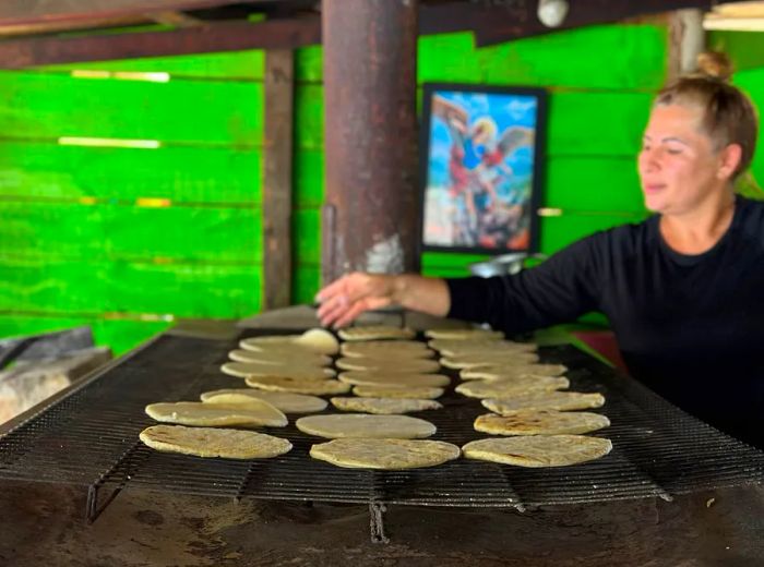 A cook tends to arepas on a large wood-fired oven.