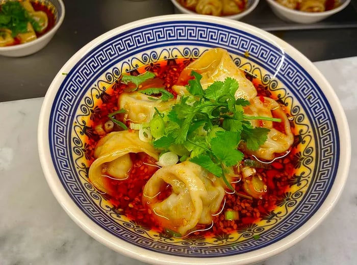 A bowl filled with dumplings drenched in red chili sauce and garnished with cilantro.