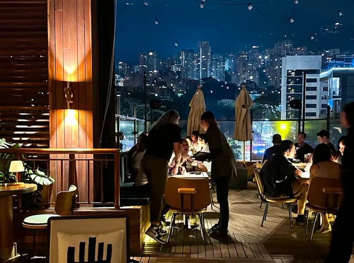 Diners enjoying a lamp-lit patio with views of Medellín at night.