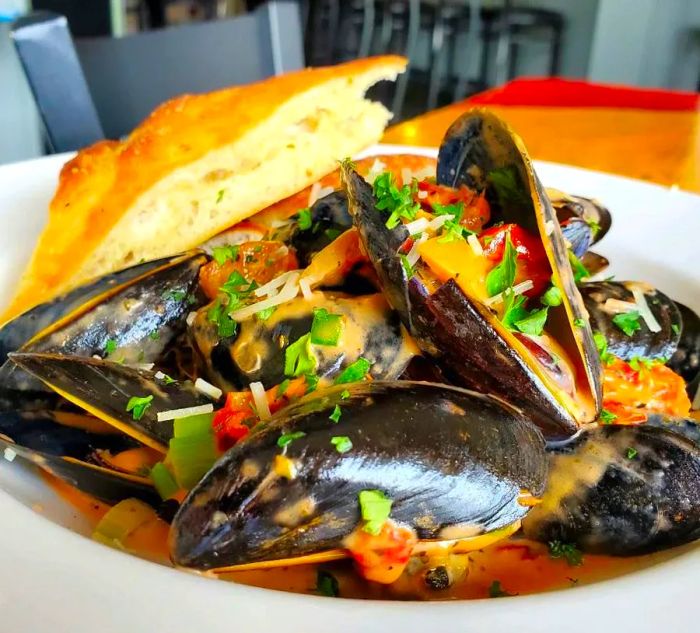 A shallow bowl filled with mussels in a savory sauce, topped with fresh herbs, accompanied by fluffy flatbread.