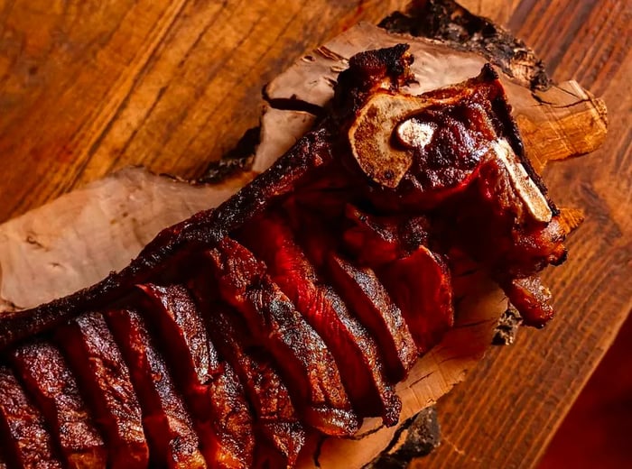 A large, sliced steak presented on a wooden serving platter.