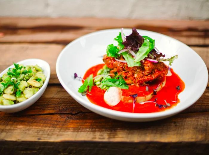 A sizable bowl of cochinita pibil bathed in a vivid red sauce, accompanied by a small dish of lima beans drizzled in green sauce.