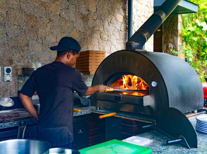 A chef expertly maneuvers a pizza paddle in a blazing pizza oven.