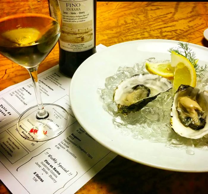 Two oysters resting on ice with lemon wedges on a pristine white plate, accompanied by a glass of crisp white wine