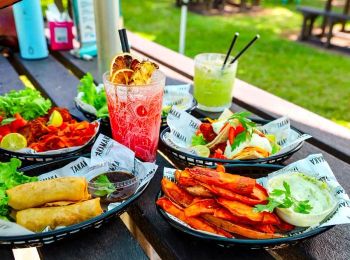 A picnic table adorned with various fried dishes and drinks, all served in paper-lined baskets.