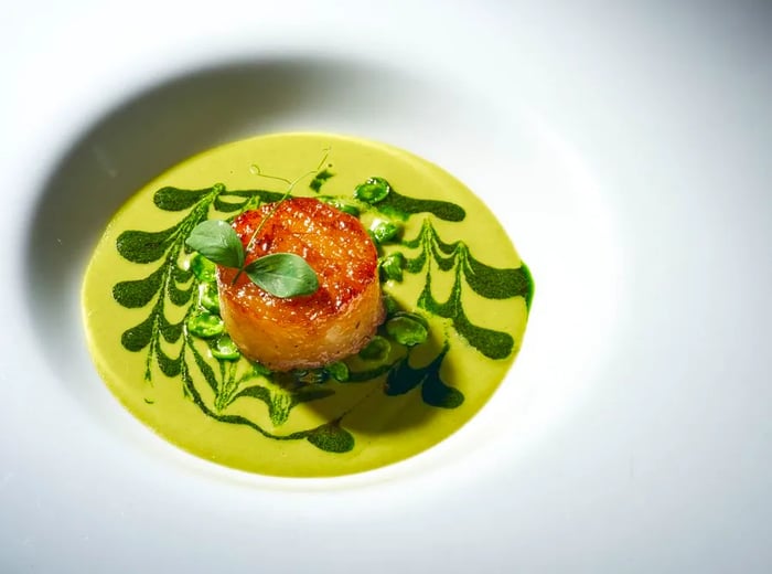 A large scallop adorned with a green zigzagged sauce.