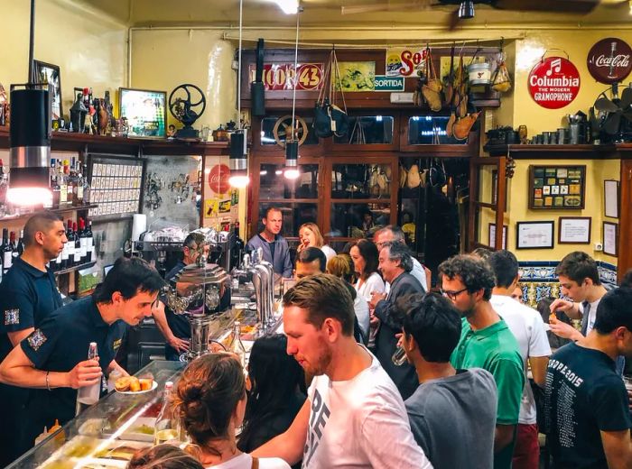 A bustling bar filled with men and women eagerly waiting for their drinks.