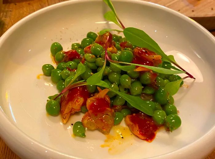 A shallow dish piled high with razor clams and topped with shelled peas.