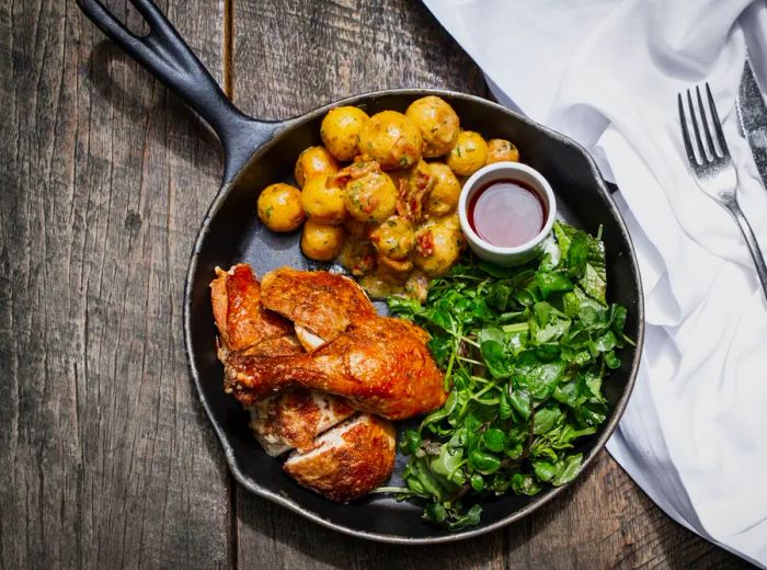 A cast iron skillet filled with roasted chicken, potatoes, and greens.