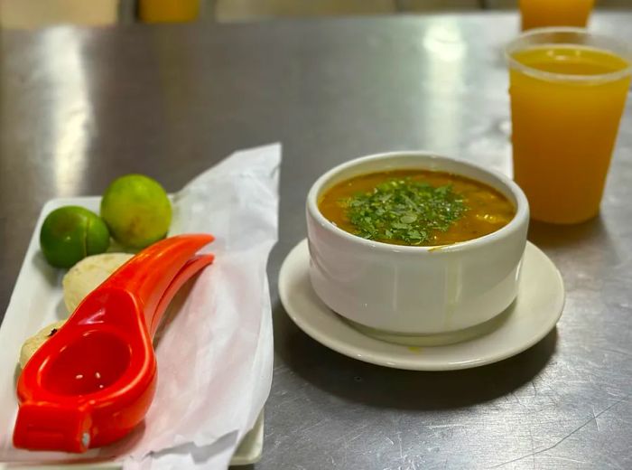 A bowl of consomme accompanied by a citrus press, small arepas, and refreshing juices.