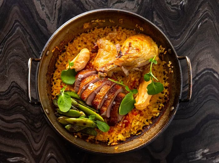 A bird's eye view of a pot filled with paella, showcasing chicken pieces and sliced meats.