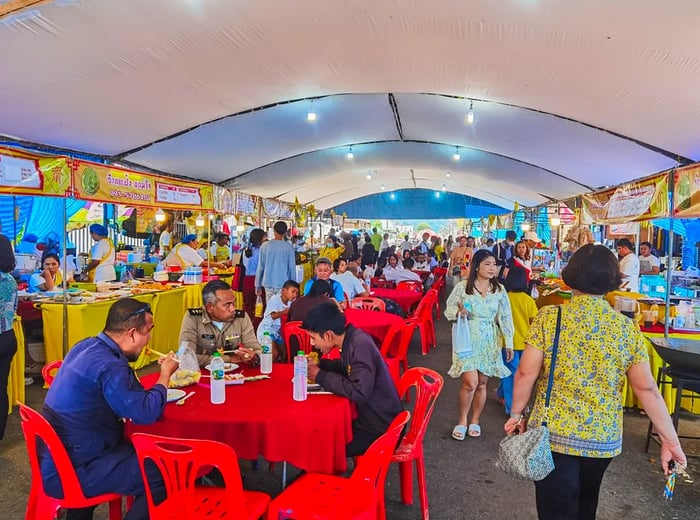 Customers stroll through food stalls and dine at tables set up in a large tent.