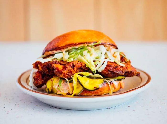 An overflowing fried chicken sandwich, garnished with an assortment of sliced vegetables.