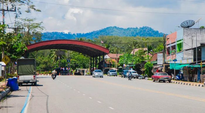 A road leading towards a spacious covered area adorned with numerous flags, set against a backdrop of mountains.