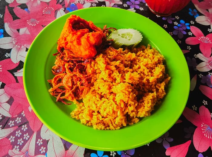 A plate featuring fried chicken, rice, crispy onions, and cucumber, set on a vibrant floral tablecloth.